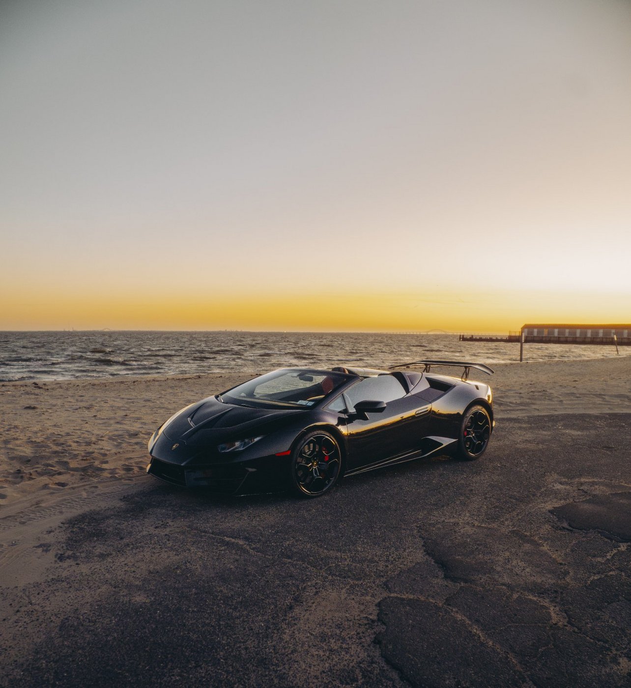 Black Lamborghini Huracán Evo Spyder with the top down at the beach at sunset