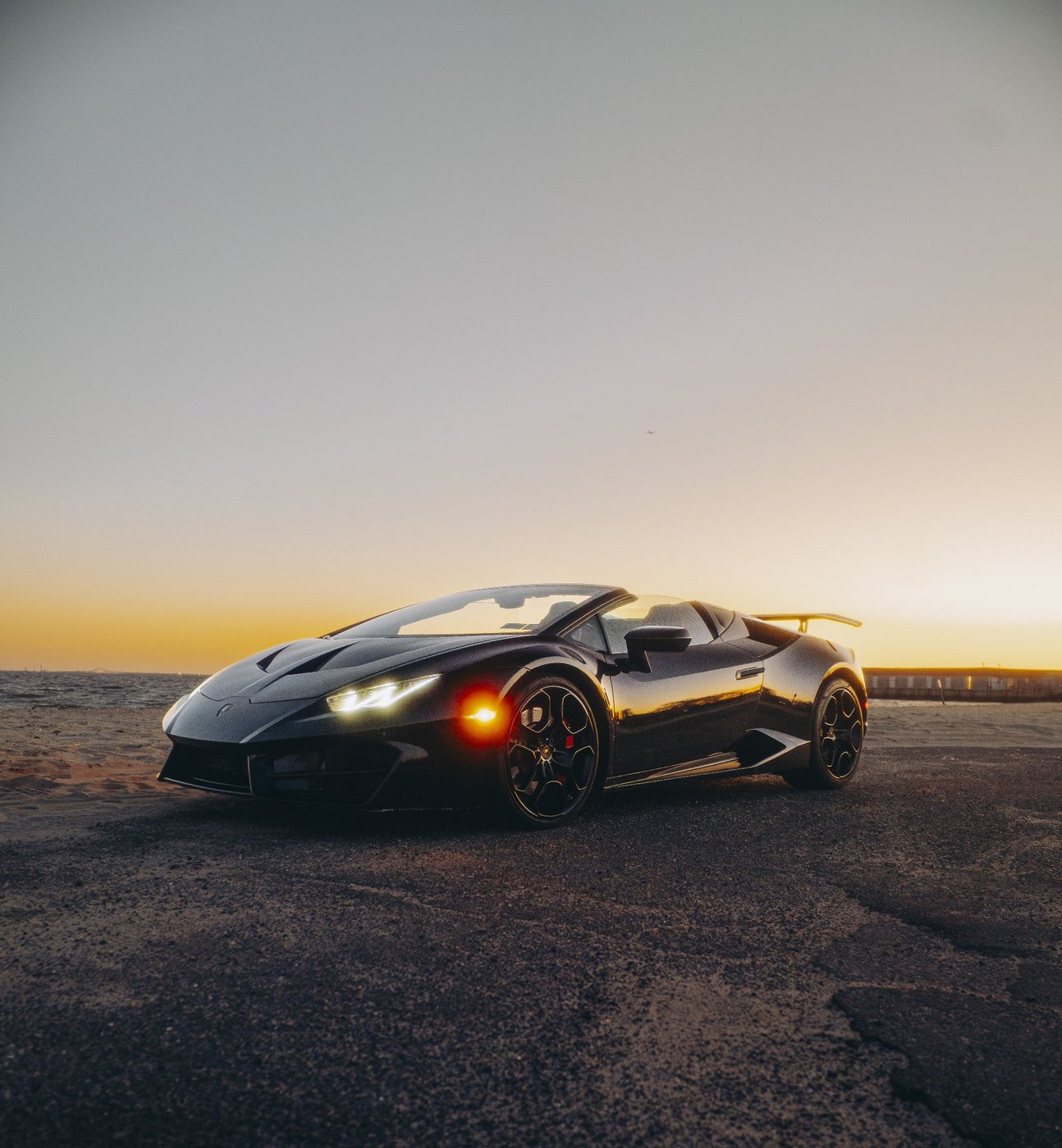 Black Lamborghini Huracán Evo Spyder with the top down shown from the front three-quarter angle at sunset