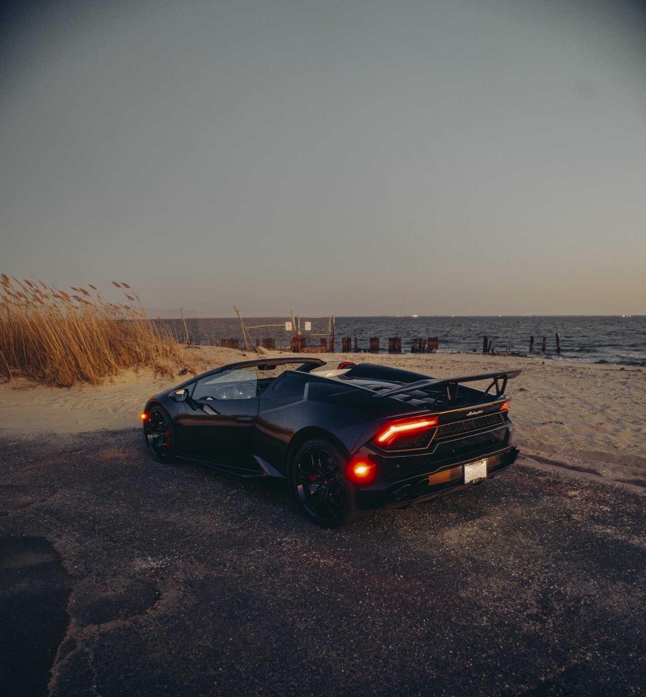 Black Lamborghini Huracán Evo Spyder shown from the rear three-quarter angle at the beach at dusk