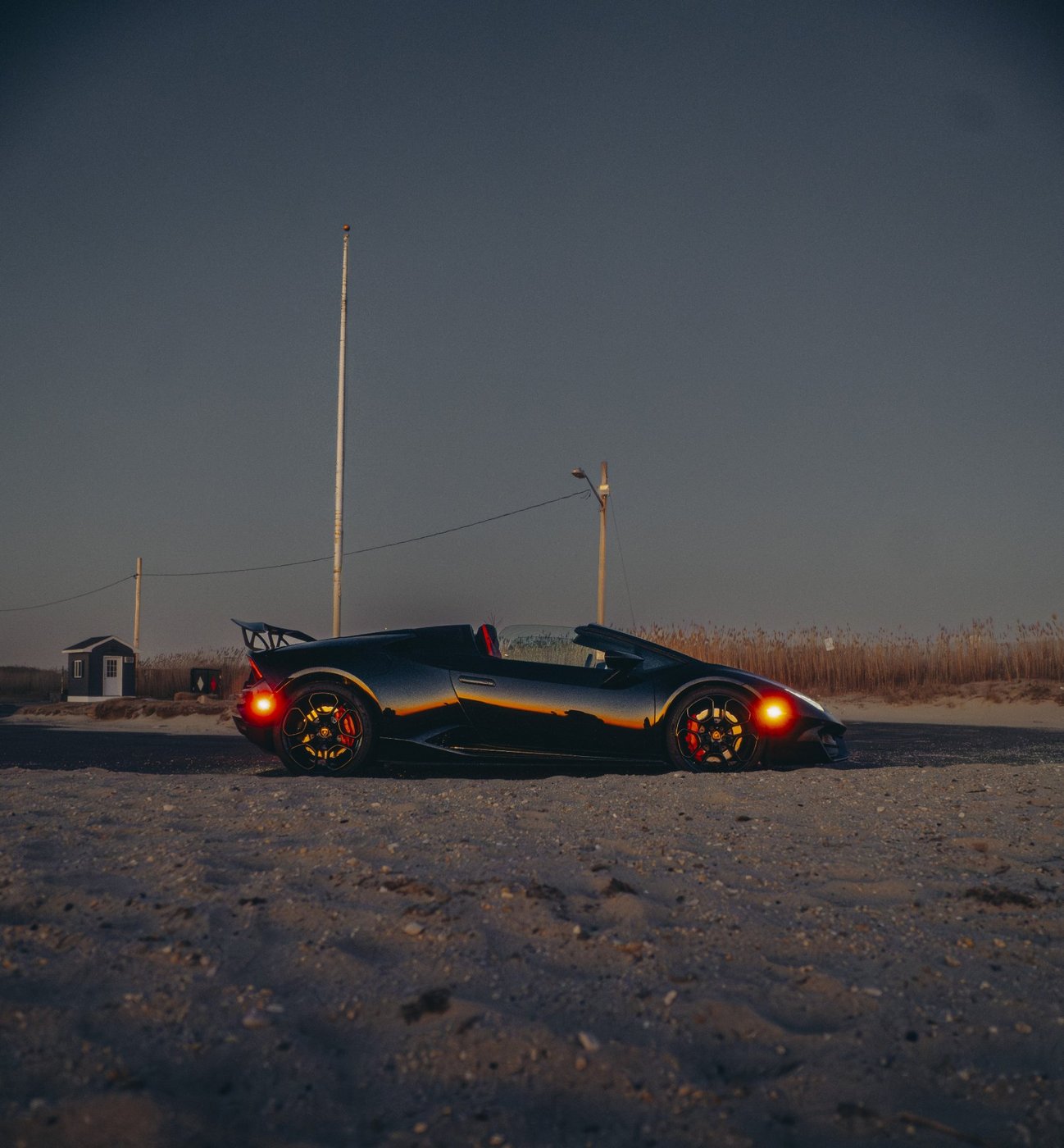 Side profile of the black Lamborghini Huracán Evo Spyder with the top down at dusk