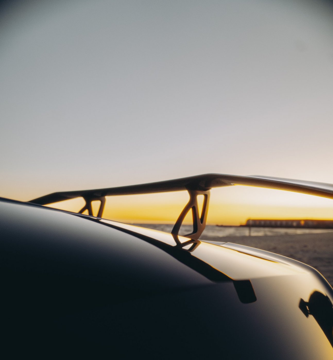 Rear wing of the black Lamborghini Huracán Evo Spyder silhouetted at sunset