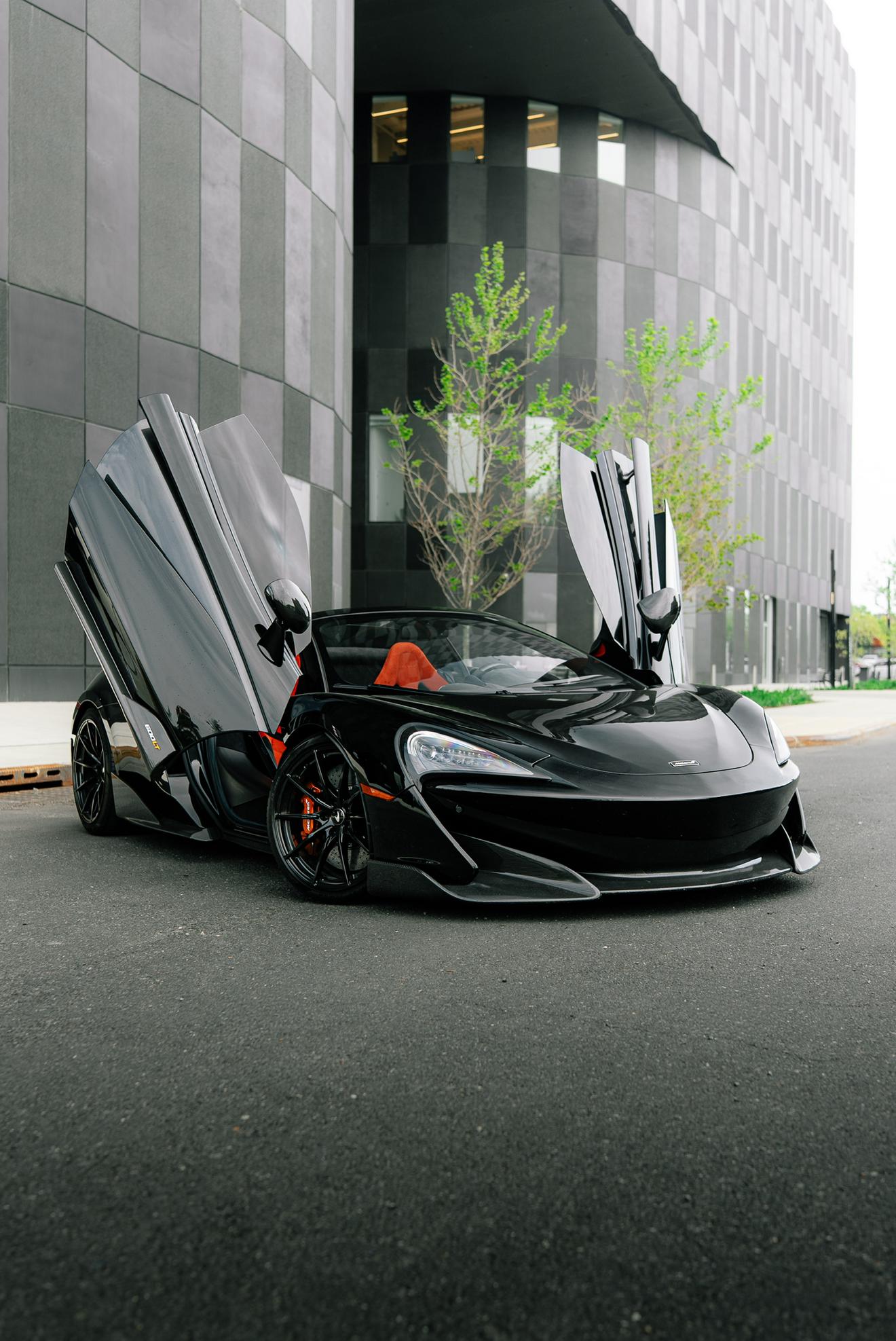 Black McLaren 600LT with its dihedral doors open shown from the front three-quarter angle