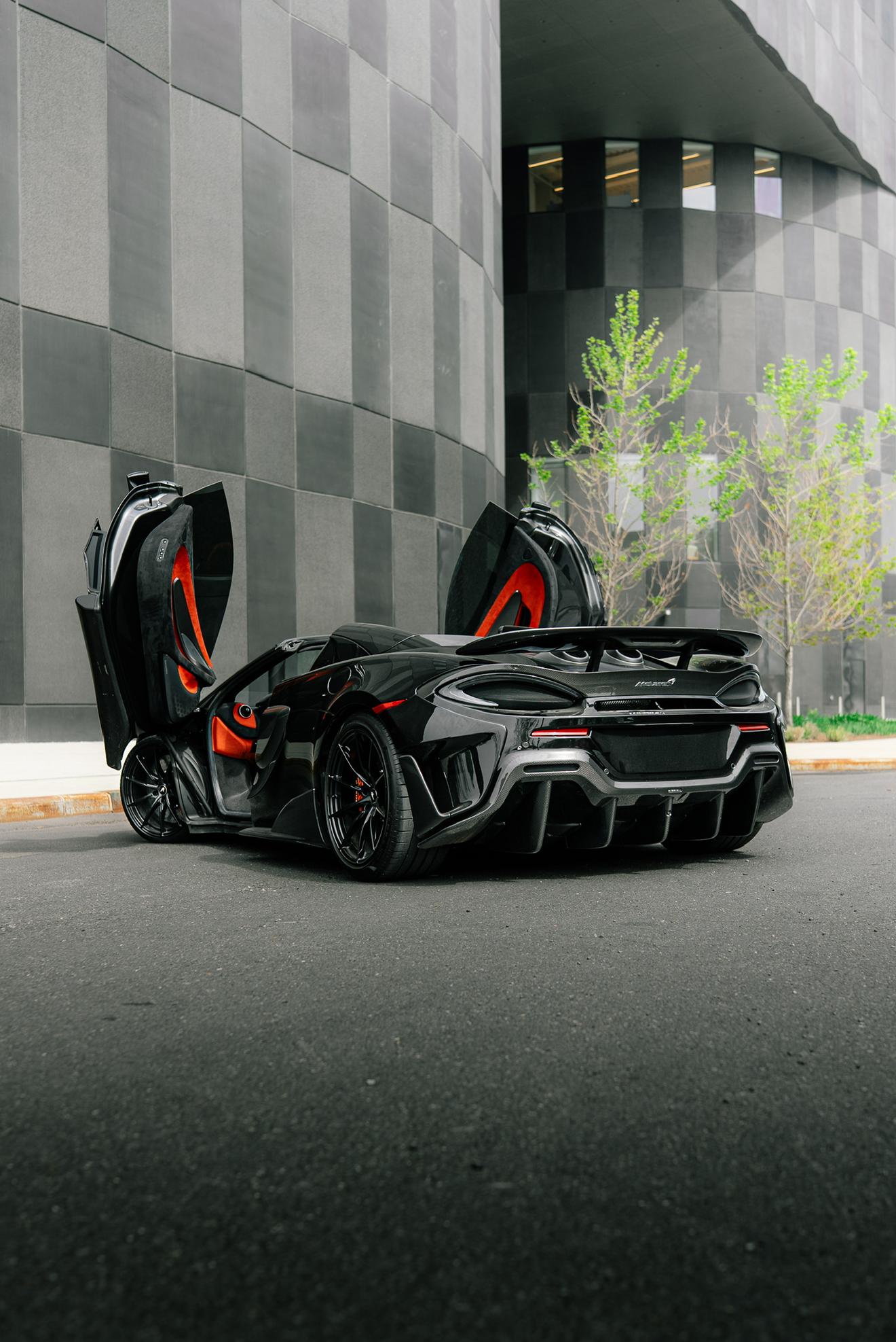 Black McLaren 600LT with its dihedral doors open shown from the rear three-quarter angle