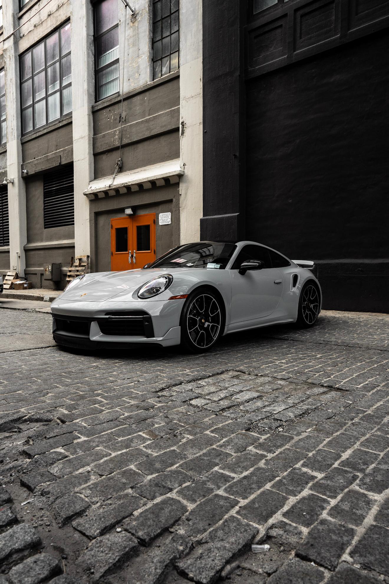 Gray Porsche 911 Turbo S shown from the front three-quarter angle on a cobblestone street