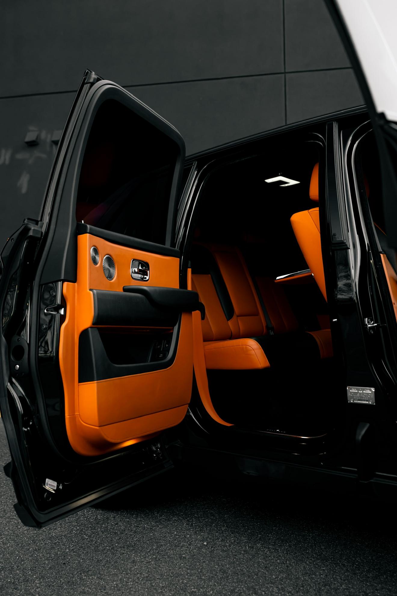 Open rear door of the black Rolls-Royce Cullinan showing the orange interior