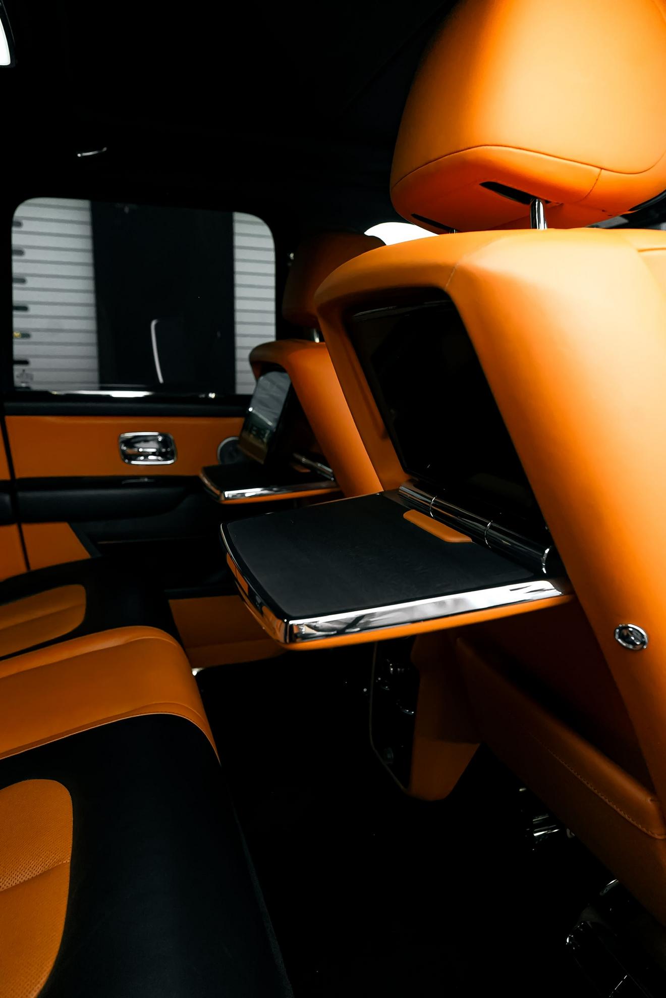 Rear cabin of the black Rolls-Royce Cullinan with orange leather seats